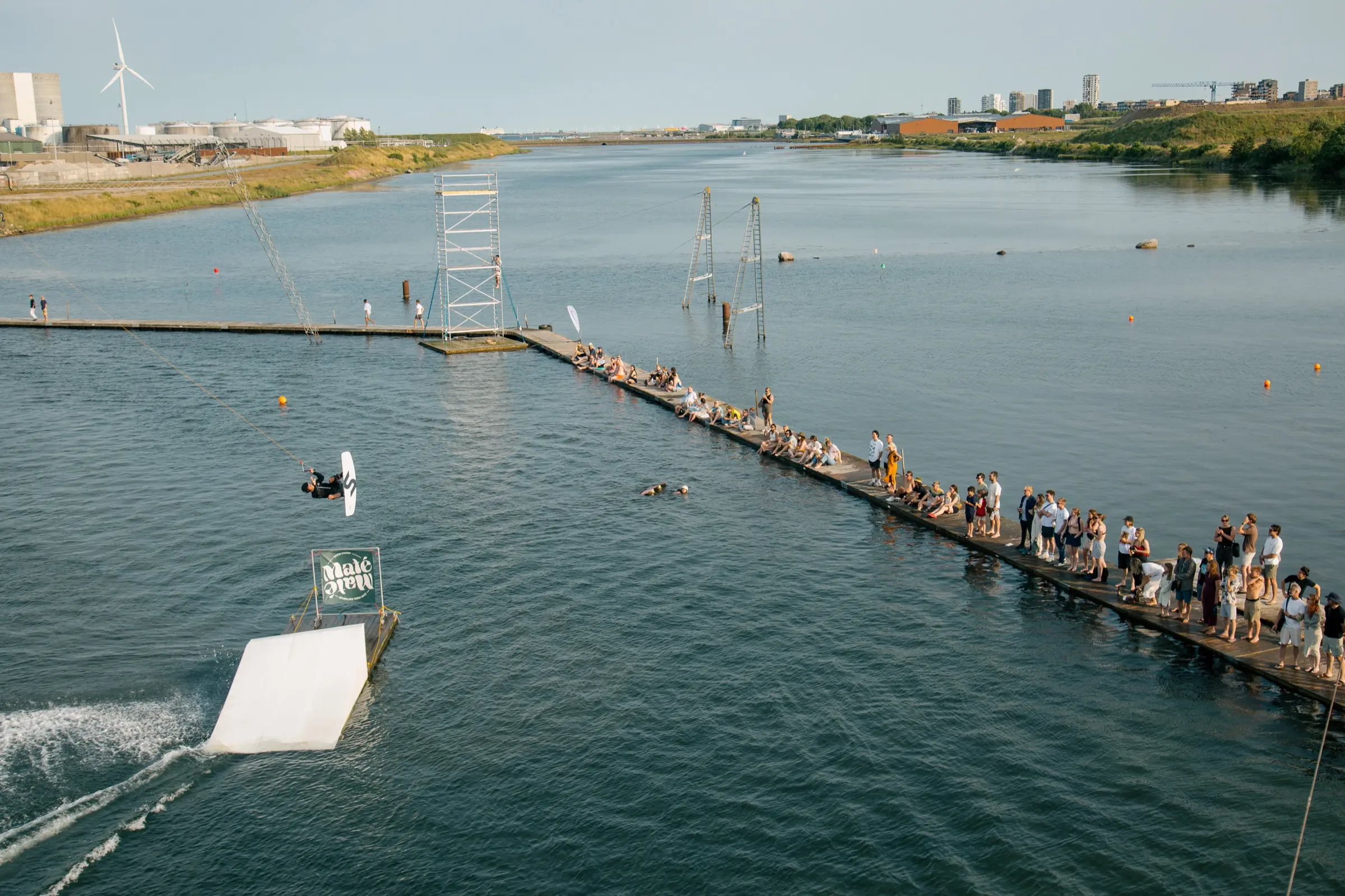 Aerial view of Copenhagen Cable Park: a rider coming off the kicker on Big Cable while the dock behind them is lined with people waiting for the next session
