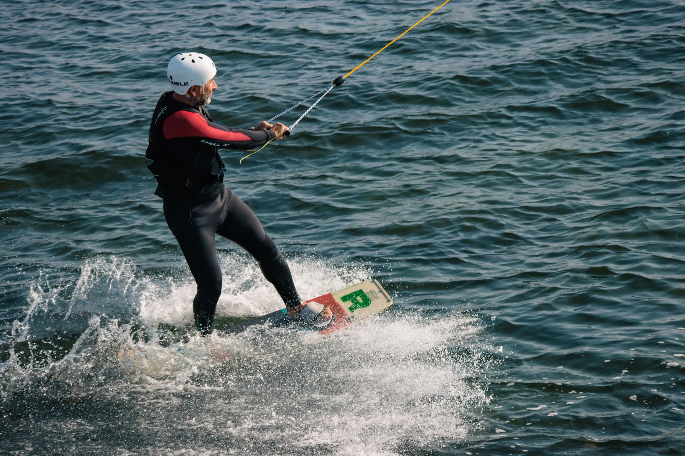 A rider on a rental board carving across open water and throwing spray
